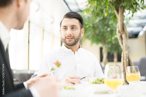 Confident young man and his business partner or colleague having talk by lunch in restaurant