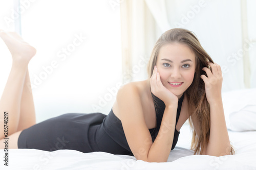 Portrait pretty young teenage girl on bed in modern apartment in the morning. She looking at you and looks happiness.
