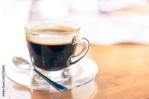A cup of hot black coffee with a small silver spoon on wooden table in bright morning light