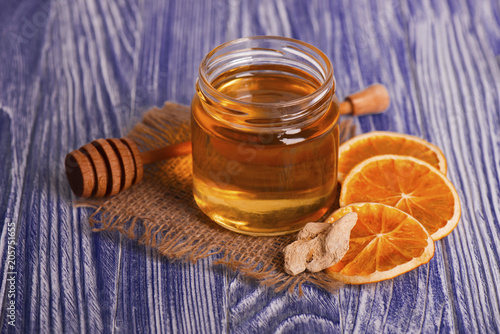 Honey in glass jar, ginger and dry slices of orange on vintage wooden background. Aromatic spices.