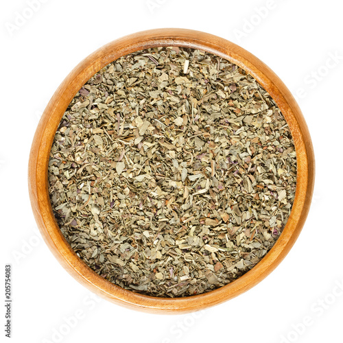 Dried basil leaves in wooden bowl. Also called great basil or Saint-Joseph's-wort. Ocimum basilicum. Chopped, culinary herb. Isolated macro food photo close up from above on white background.