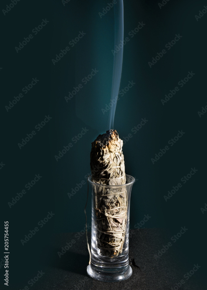 Sage with smoke burning in a glass against a black background.