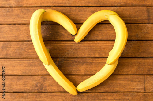 Yellow bananas are in the shape of a heart on a wooden table
