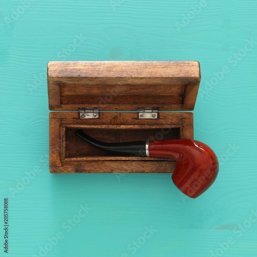 Top view of old smoking pipe and vintage wooden box over blue background.