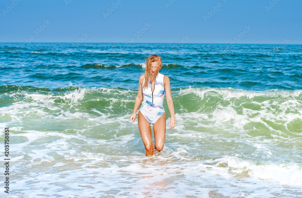 Summer. Beautiful tanned woman in swimsuit is coming out of the ocean Summer. Beautiful tanned woman in swimsuit is coming out of the ocean