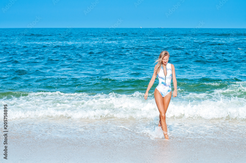 Summer. Beautiful tanned woman in swimsuit is coming out of the ocean