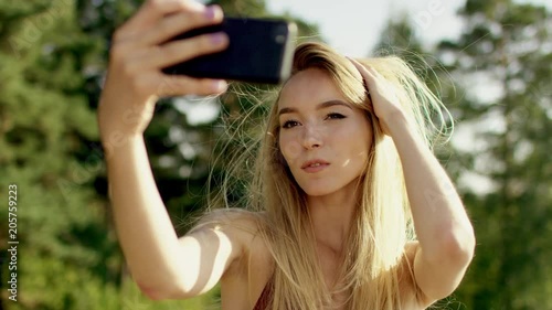 beautiful blonde brown-eyed long-hair girl making selfi with her phone and play with her hair in brown swimsuit and bikini a background of nature