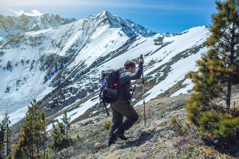 Hiker with trekking poles stands in the snowy mountains at the foot of the peak. Concept of travel and achieve the goal