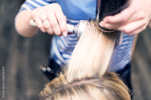 Blowing of blonde hair in hairdressing salon. Brushing hair detail.