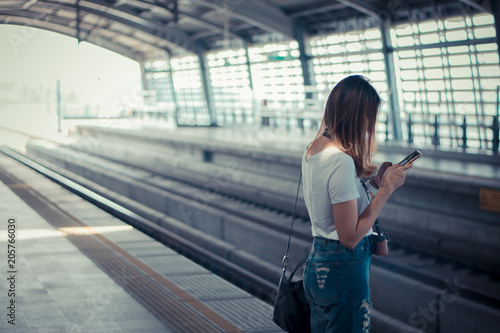 Woman waiting on the station platform and using smart phone at the airport link station. © grooveriderz