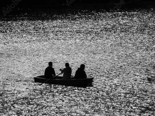 Black and white tone of silhouette landscape of three men and the boat in the lake.