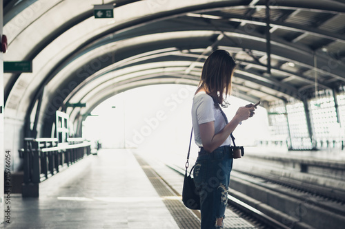 Woman waiting on the station platform and using smart phone at the airport link station.