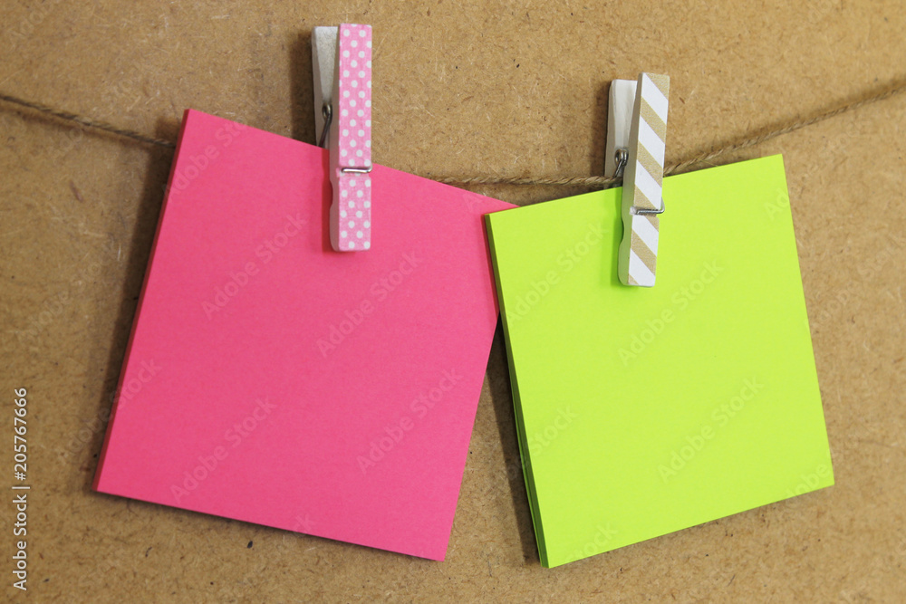  Hoja de papel de color rosa y verde (posit), sujeto con pinzas de colores y dibujos, en una cuerda a la pared de corcho Stock Photo