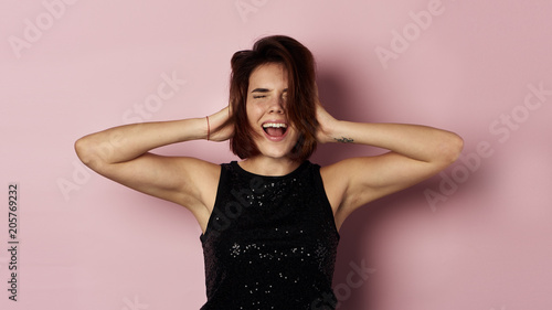 Young emotional female screaming, touching her head. Studio portrait over pink background. 