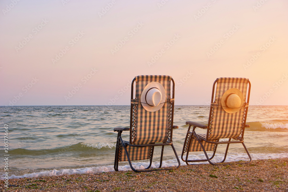 Checkered beach chairs on the seashore with sun hats.