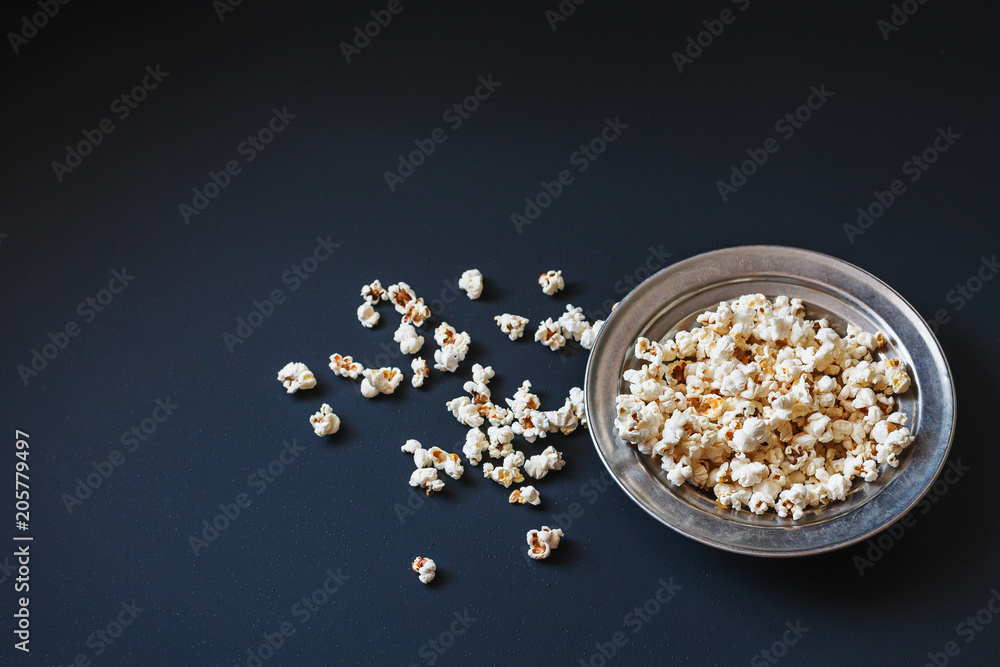 Top view of popcorn in a metallic plate on a matte black surface Top view of popcorn in a metallic plate on a matte black surface