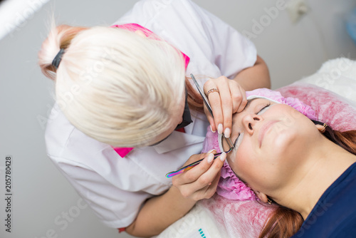 Permanent makeup. Eyelash Extension Procedure. Woman Eye with Long Eyelashes. Professional stylist lengthening female lashes. Eyelash extension procedure - master and a client in a beauty salon