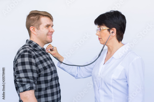 Doctor listening to cheerful young patient's chest with stethoscope over white background