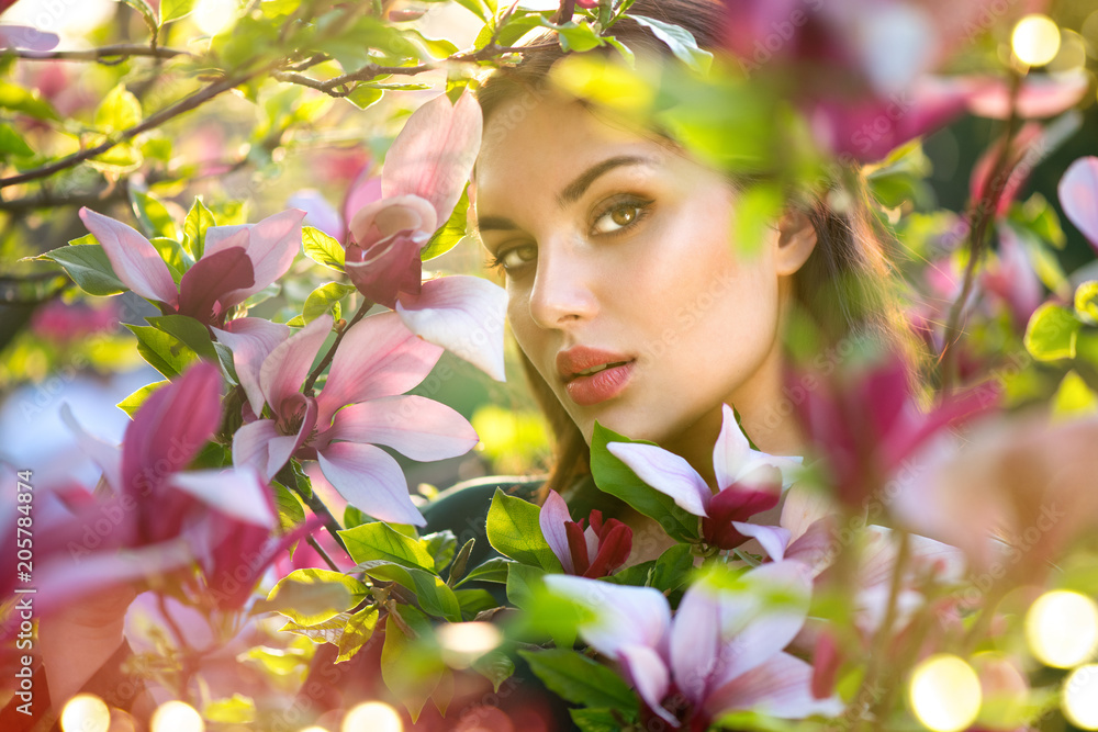 Naklejka premium Blooming magnolia trees. Beauty young woman touching and smelling spring magnolia flowers. Happy beautiful girl enjoying nature