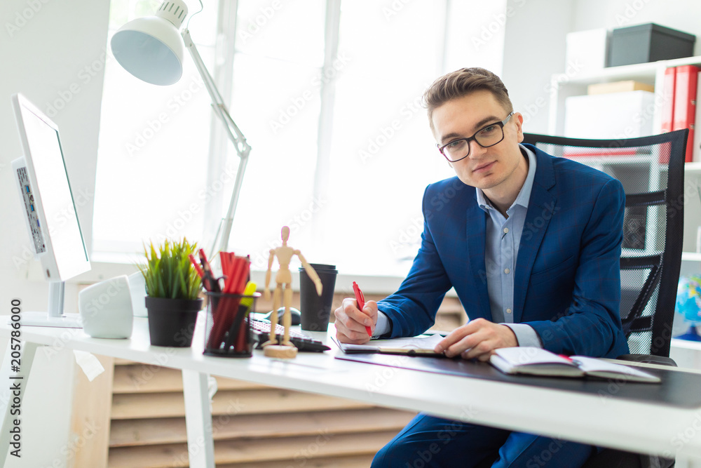 A young man sits at a table in the office, holds a red pen in his hand and works with documents. A young man sits at a table in the office, holds a red pen in his hand and works with documents.