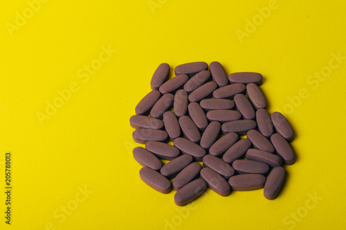 A handful of oval, purple tablets lie on a yellow background.