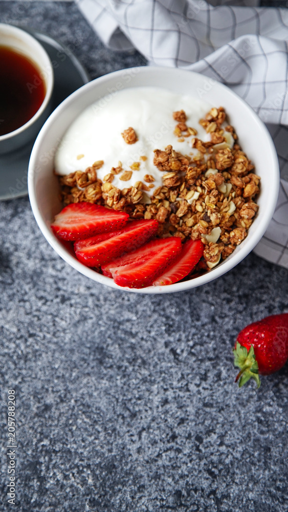 Perfect breakfast: crunchy granola with yoghurt and strawberries with a cup of black coffee on gray bakcground. Flat lay with copy space Perfect breakfast: crunchy granola with yoghurt and strawberries with a cup of black coffee on gray bakcground. Flat lay with copy space