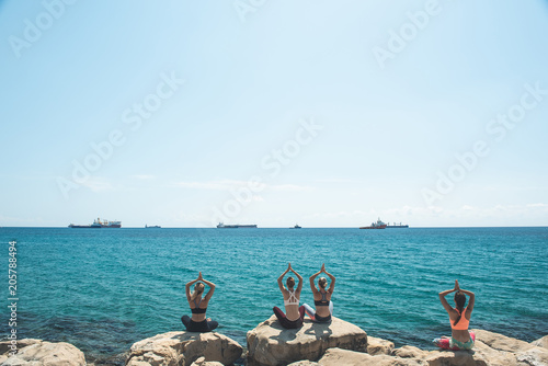 Attractive females arising hands up while meditating near endless sea. Ships swimming there. Copy space. Peace in soul concept