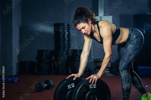 Beautiful sexy woman with good figure and attractive ass poses in the gym. The girl in the top and obblegivayuschih pants, leggings are leaning their hands on weighting agents, pancakes for the bar.