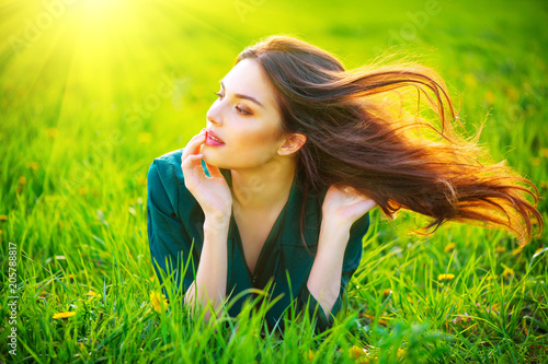 Beauty woman lying on the field enjoying nature. Beautiful brunette girl with healthy long flying hair. Summer green grass