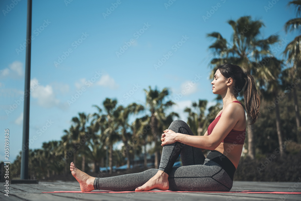 Full length side view orderly lady stretching body while sitting on street. Serene lady demonstrating composure during physical exercise concept
