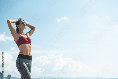 Portrait of smiling lady resting against blue sky after working out. Happy girl practicing gymnastic exercise concept