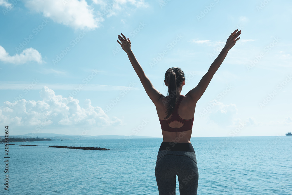 I am free. Female gesticulating hands while turning back to camera. She looking at blue ocean. Sport in open air concept I am free. Female gesticulating hands while turning back to camera. She looking at blue ocean. Sport in open air concept