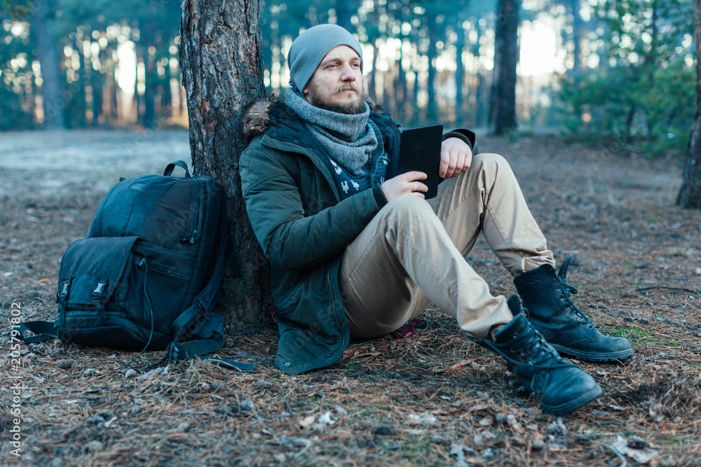 adult handsome Male traveler Sits On autumn pine forest Near tree, Holding At Tablet Recreation Resting Travel Destination Concept adult handsome Male traveler Sits On autumn pine forest Near tree, Holding At Tablet Recreation Resting Travel Destination Concept
