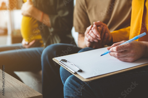 Close up of female arm signing a surrogacy agreement. Man is holding wife hand with fondness. Pregnant woman is sitting on background  photo