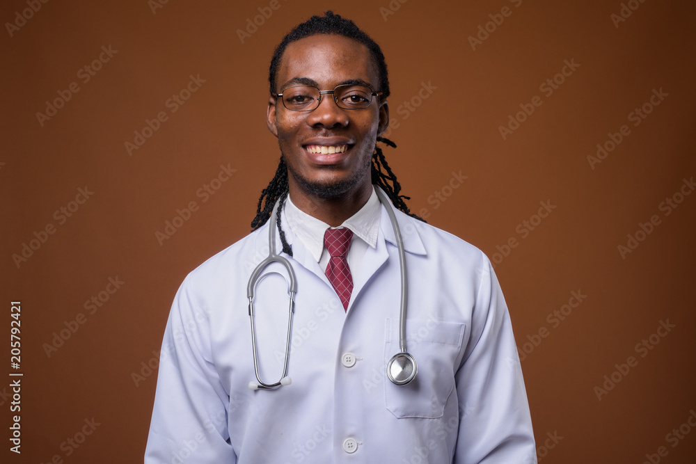 Young handsome African man doctor against brown background Young handsome African man doctor against brown background