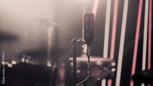 Microphone in recording Studio or concert hall close-up, with drum set on background out of focus.