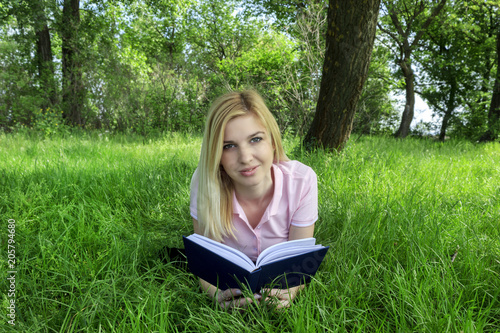 blonde is reading a book in a park on the grass