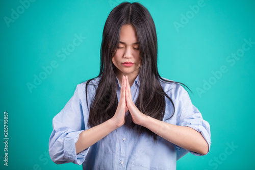 Young Corean woman bowing her head with folded hands in a traditional greeting or prayer, upper body isolated on blue