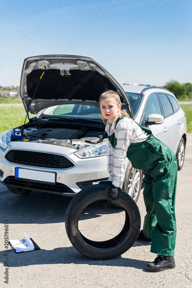 Woman with spare wheel near broken car