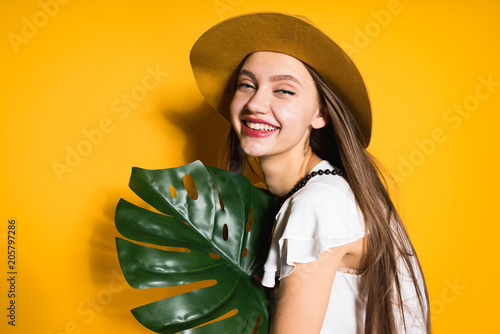 happy young girl model in a fashionable hat holds a green leaf and poses, laughs