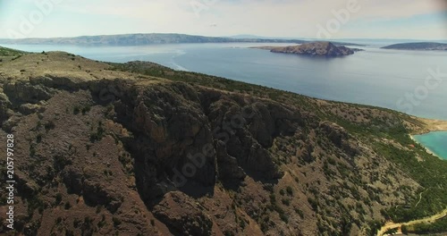 wide aerial shot of the croatian rocky coastline with the typical pine flora. the camera moves forward and tilts down with foucs on a big rocky cliff. many rocky islands in the background
