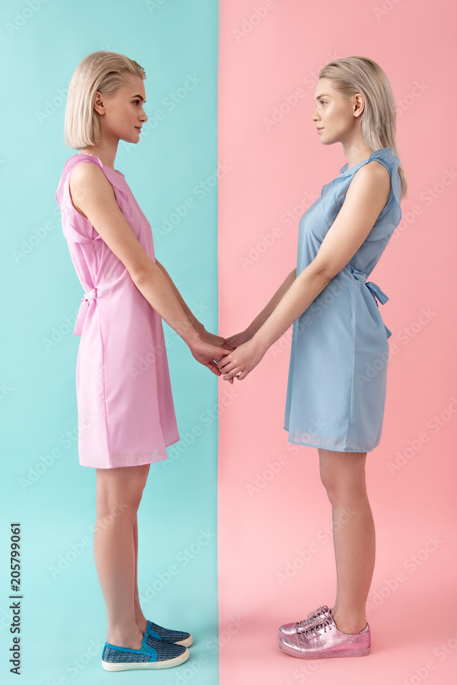 Side view profile of serious women standing in dresses, holding hands and looking at each other