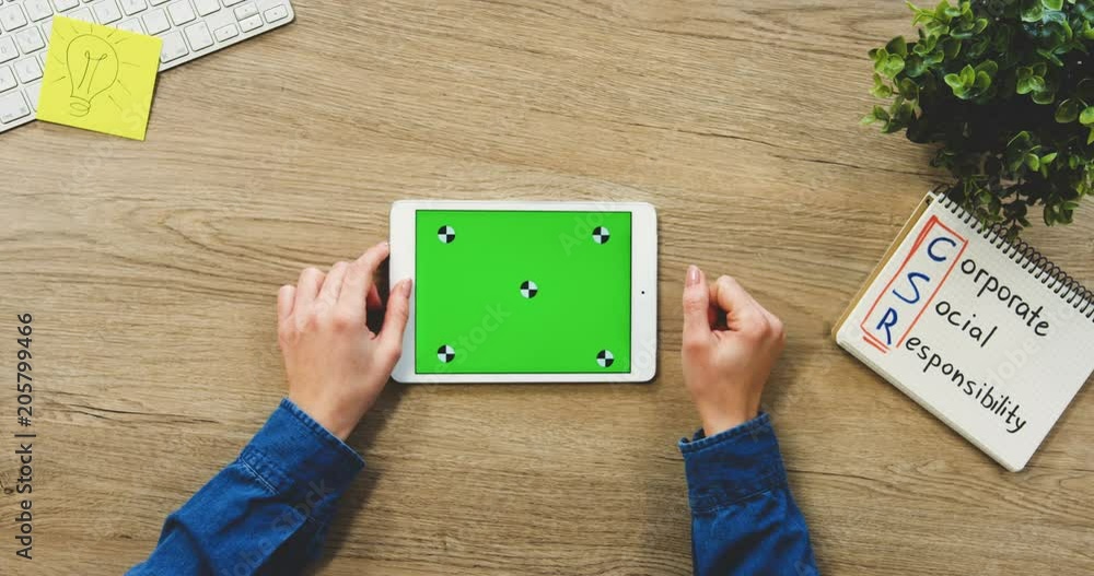 Close up of the woman's hands using the white horizontal tablet computer with a green screen on the wooden office table. Corporate Social Responsibility. Chroma key. Top view. Tracking motion Close up of the woman's hands using the white horizontal tablet computer with a green screen on the wooden office table. Corporate Social Responsibility. Chroma key. Top view. Tracking motion