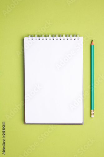 Blank notebook with pencil on green pastel background. Flat lay concept.. Vertical view