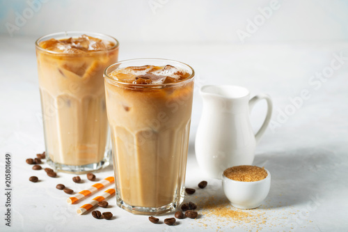 Ice coffee in a tall glass with cream poured over and coffee beans. Cold summer drink on a light blue background