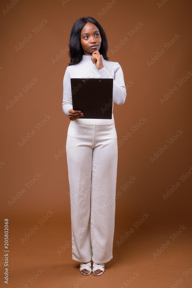 Young beautiful African Zulu businesswoman against brown backgro Young beautiful African Zulu businesswoman against brown backgro