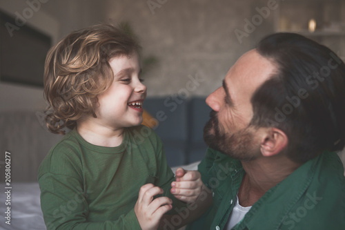 Side view laughing son talking with outgoing father while looking at him in apartment