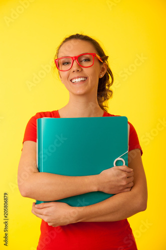 Beautiful young student woman holds folder over yellow background