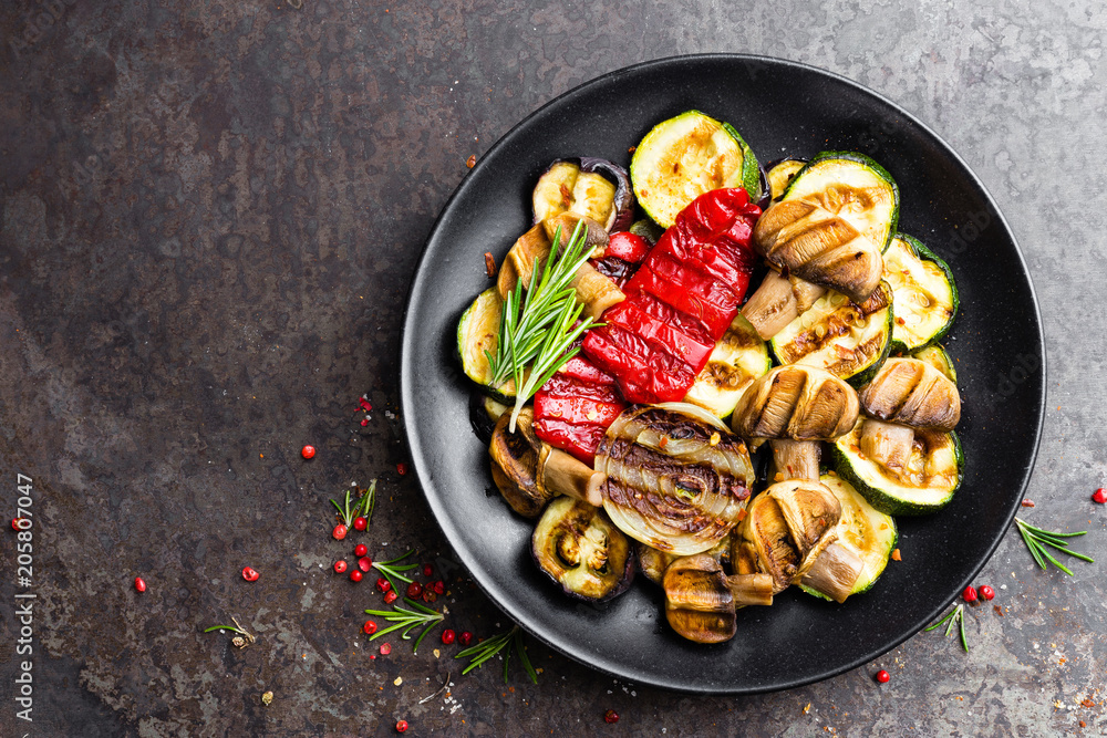 Grilled vegetable salad. Salad of barbecued zucchini, eggplant, sweet pepper, onion and mushrooms on black plate Grilled vegetable salad. Salad of barbecued zucchini, eggplant, sweet pepper, onion and mushrooms on black plate
