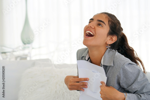 Young woman enjoying good news in writing. The girl reads a letter with good news sitting on the couch. An euphoric girl is happy after reading good news in a written letter, approving a loan. photo